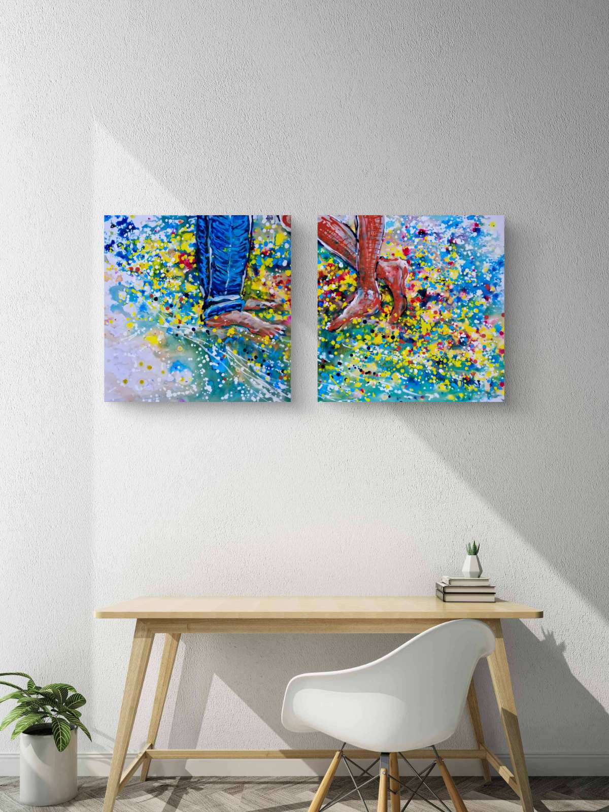 Love affair diptych original abstract painting set by contemporary artist TRAXI, depicting playful feet on the beach with vibrant fluid acrylic colors. Two square abstract canvas prints with colorful brushstrokes of blue, yellow, green, and red hang on a white wall above a light wood desk and a white chair.