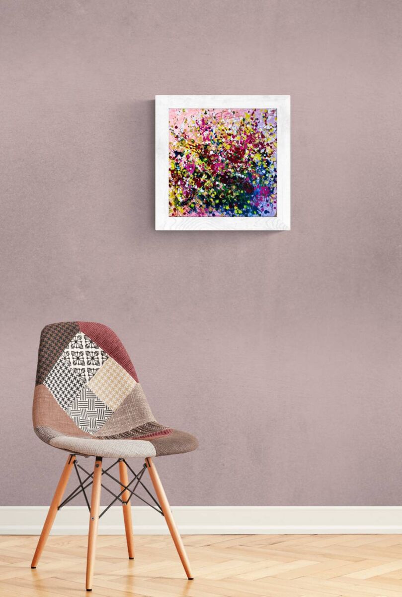 Original abstract painting Summer Garden Flowers by Diana Dimova TRAXI, featuring a colorful floral bouquet in vibrant yellow, pink, and orange tones. A colorful abstract floral painting in a white square frame, displayed on a textured mauve-gray wall above a modern patchwork upholstered chair with wooden legs.