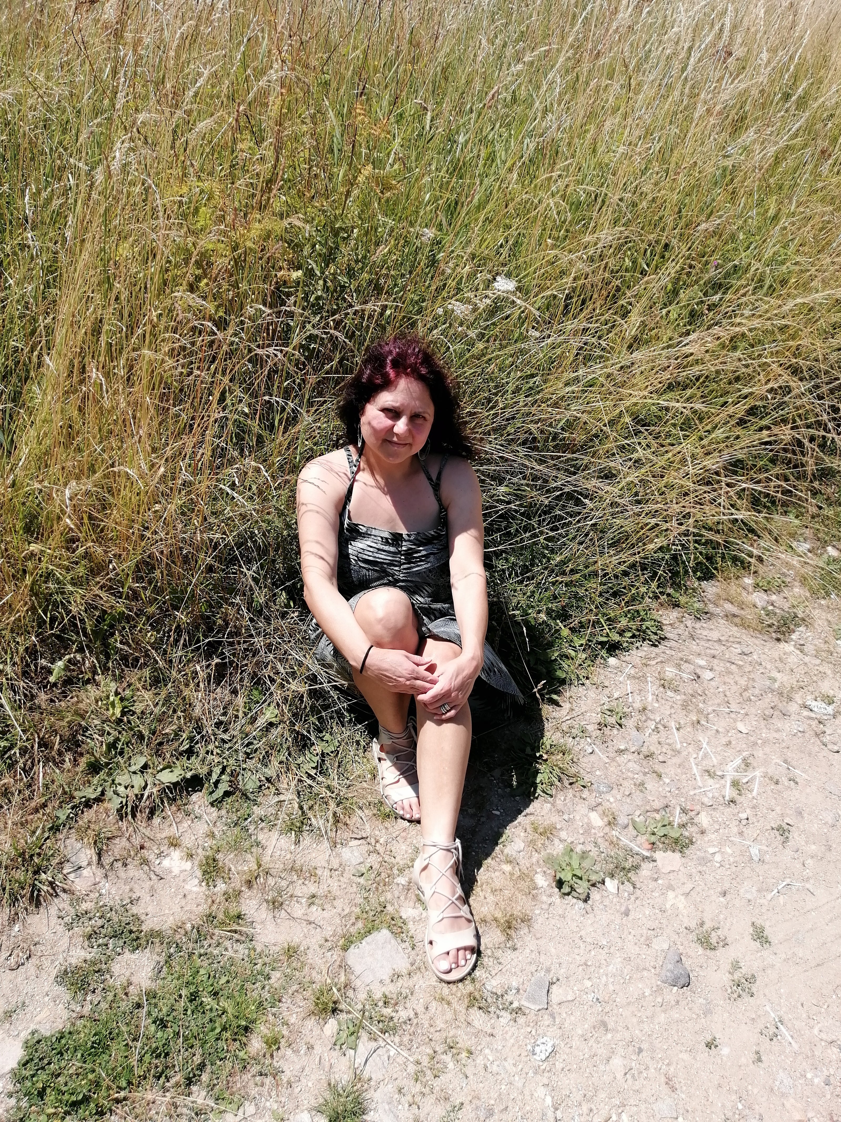 LIFE IS WONDERFUL — A Virtual Fine Art Solo Exhibition by Diana Dimova TRAXI. Art Project inspired by Nature, exploring Time.

 A woman with dark hair sits on the ground in a field of tall dry grass, wearing a black and gray patterned camisole top and gray shorts.