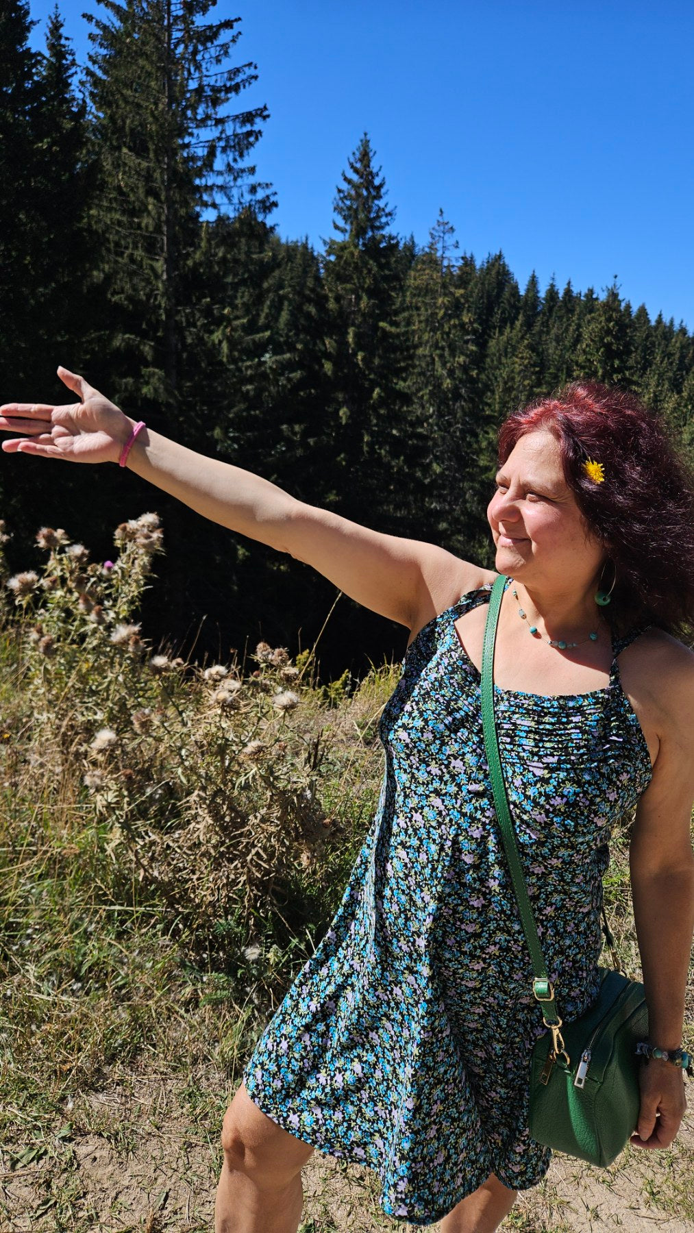 LIFE IS WONDERFUL — A Virtual Fine Art Solo Exhibition by Diana Dimova TRAXI. Art Project inspired by Nature, exploring Time.

A woman with red hair wearing a blue and green floral sleeveless dress stands outdoors in a sunny forest clearing, pointing to the left with her arm extended. She is carrying a green crossbody bag.