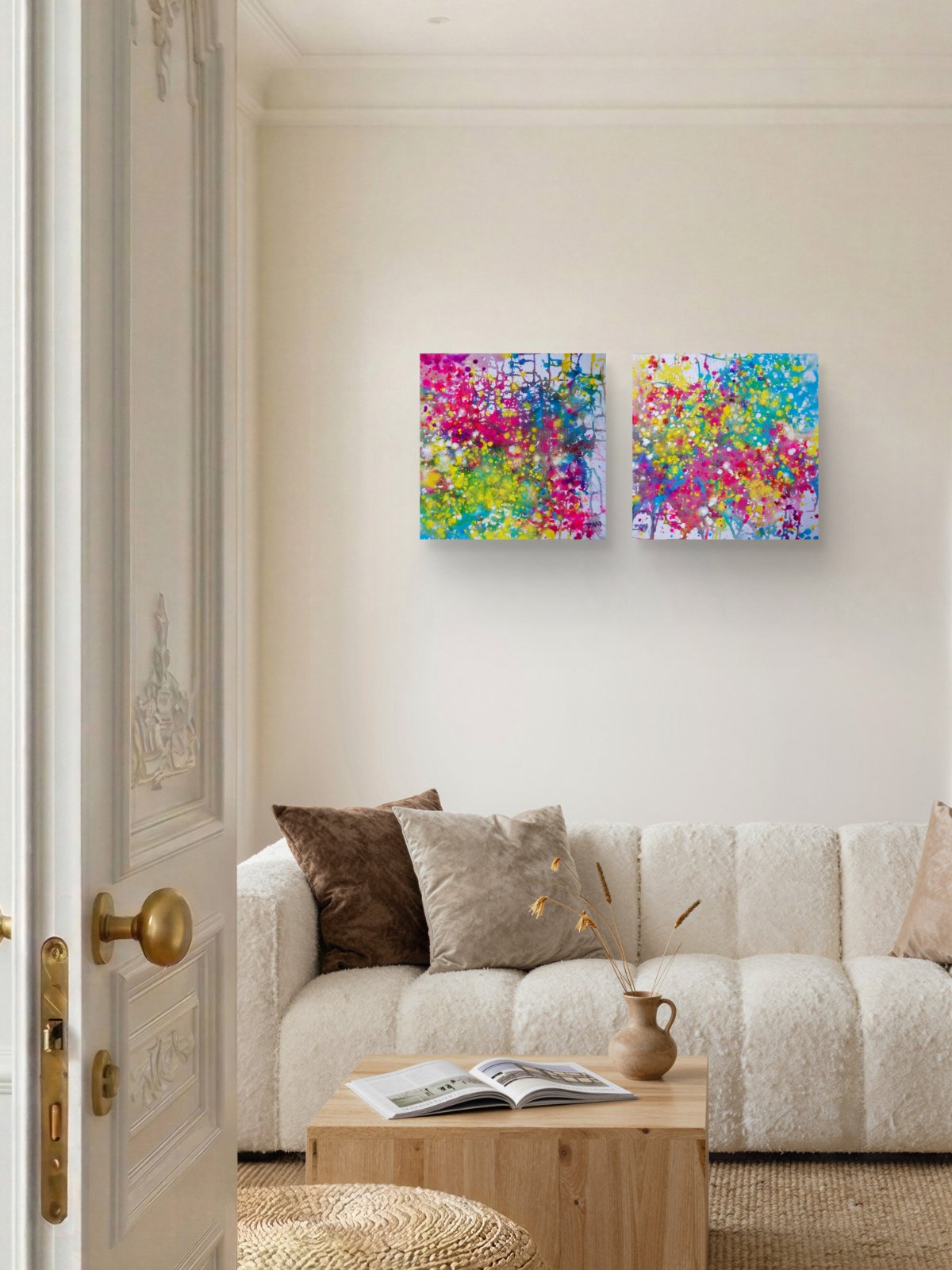 Paintings of Happiness Dyptich by Diana Dimova TRAXI,  Colorful Abstract Art Set. Two square abstract canvas prints with vibrant multicolor paint splatters hang on a cream wall above a white textured sofa in a modern living room setting.