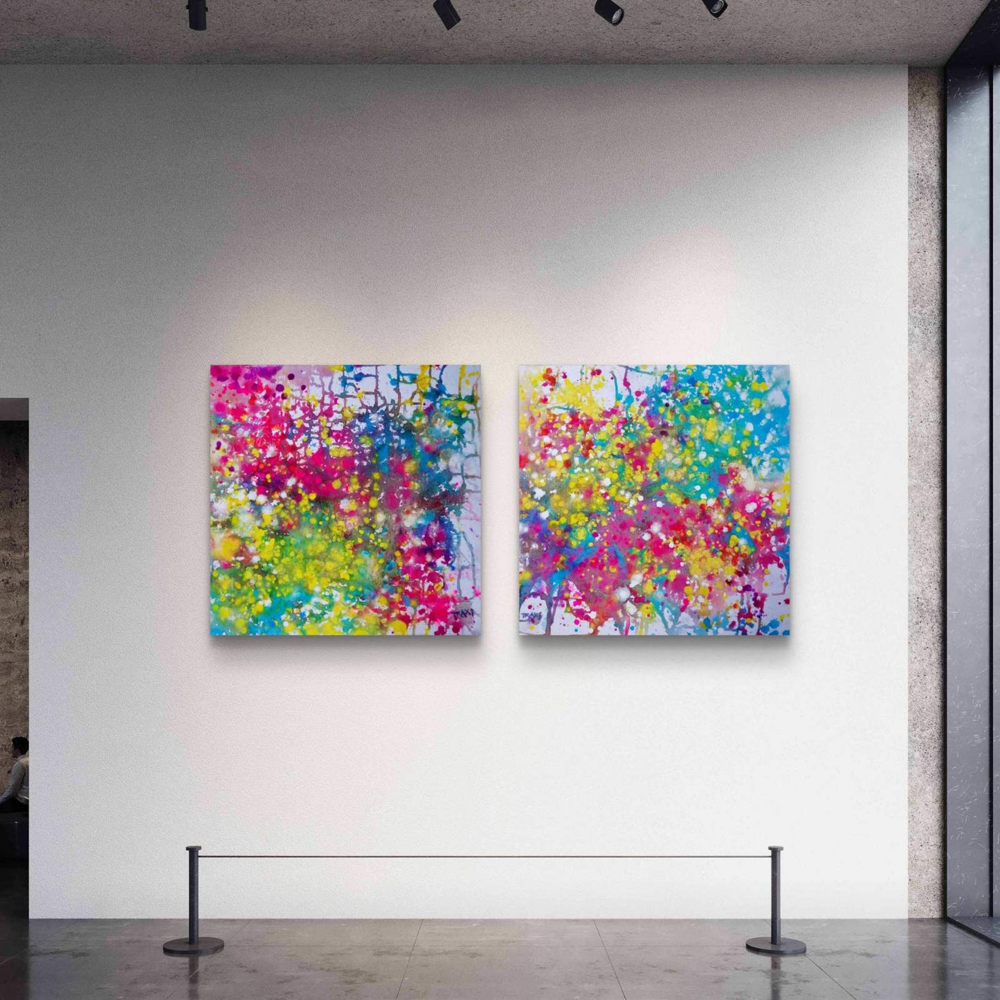 Paintings of Happiness Dyptich by Diana Dimova TRAXI,  Colorful Abstract Art Set. Two square abstract wall art canvases with vibrant splashes of pink, yellow, blue, green, and white, displayed side-by-side on a white gallery wall with gallery stanchions below.