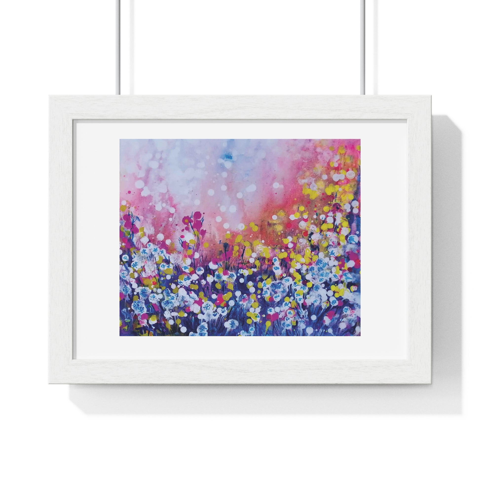Abstract landscape in pink and blue with dandelions framed art print by contemporary artist TRAXI, featuring a magical sunrise scene on archival matte paper. A framed floral art print featuring a colorful painted field of flowers in pink, purple, blue, yellow, and white tones, presented in a white frame against a clean white background.