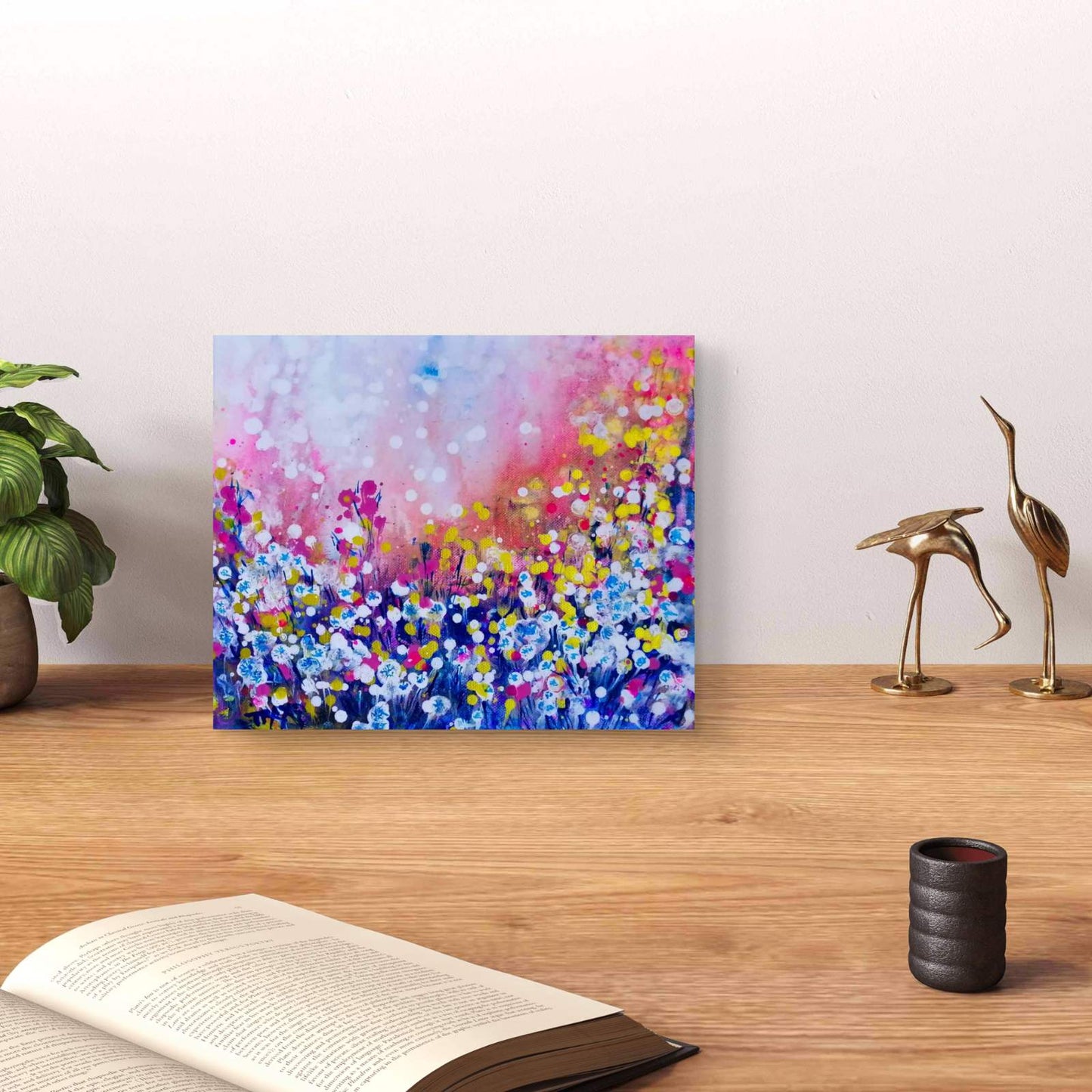 Original Painting, Life is Wonderful, Abstract Landscape, Dandelions Art, Pink and Blue Abstract, Small Art Gift, Diana Dimova TRAXI, Romantic Painting, Contemporary Fine Art, 30x25 cm A colorful abstract floral canvas print displayed on a wooden table in a styled room setting, next to a potted plant, an open book, and two gold bird figurines.