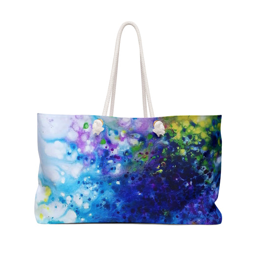 Aromatic lavender symphony beach bag featuring vibrant wearable art inspired by the painting Aromatic Lavender Symphony by Diana Dimova TRAXI. A tote bag with a colorful abstract watercolor print in shades of blue, purple, green, and white, featuring two cream-colored rope handles, shown against a plain white background.