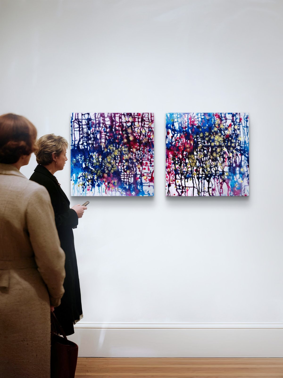 Award-winning original abstract diptych Greed and Fear by Diana Dimova TRAXI, fluid acrylic pouring in white, blue, rose and gold tones Two abstract canvas paintings with vibrant blue, purple, pink, and white paint drips hang on a white gallery wall, with two people standing in the foreground observing them.