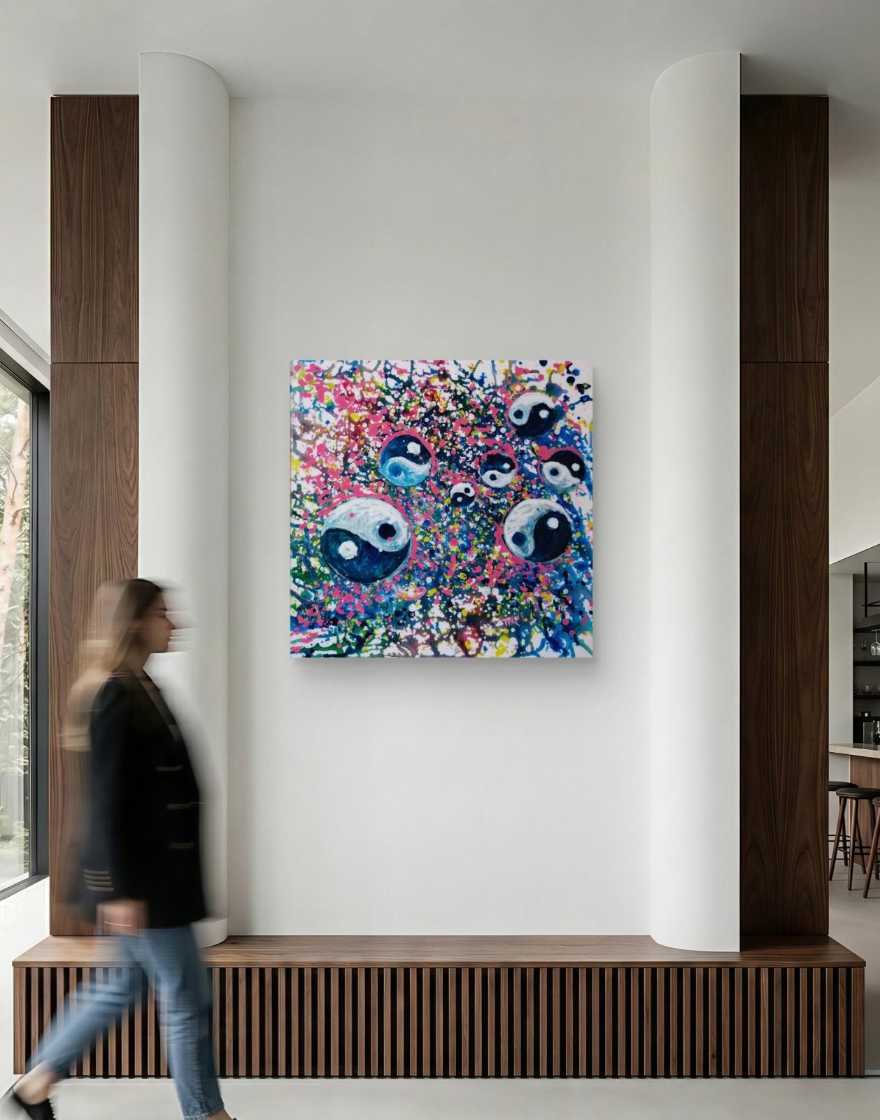 Yin Yang spiritual abstract painting titled Events of Life by Diana Dimova TRAXI featuring a circular blue, white, and soft pink composition for modern luxury interiors. A colorful abstract canvas print featuring three stylized blue and white eyes surrounded by vibrant splatters, displayed on a white wall in a modern interior setting with a blurred person walking past.