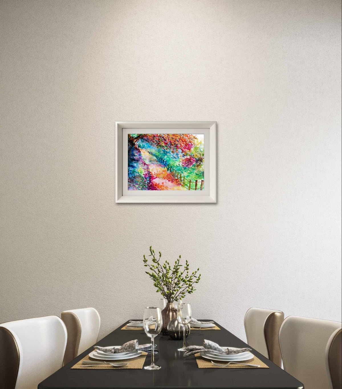 Colorful Autumn Landscape, original fall watercolor painting with an autumn path on paper by contemporary artist TRAXI. A framed abstract colorful painting hangs on a light beige wall above a dining table set with white chairs, plates, and a vase with greenery.