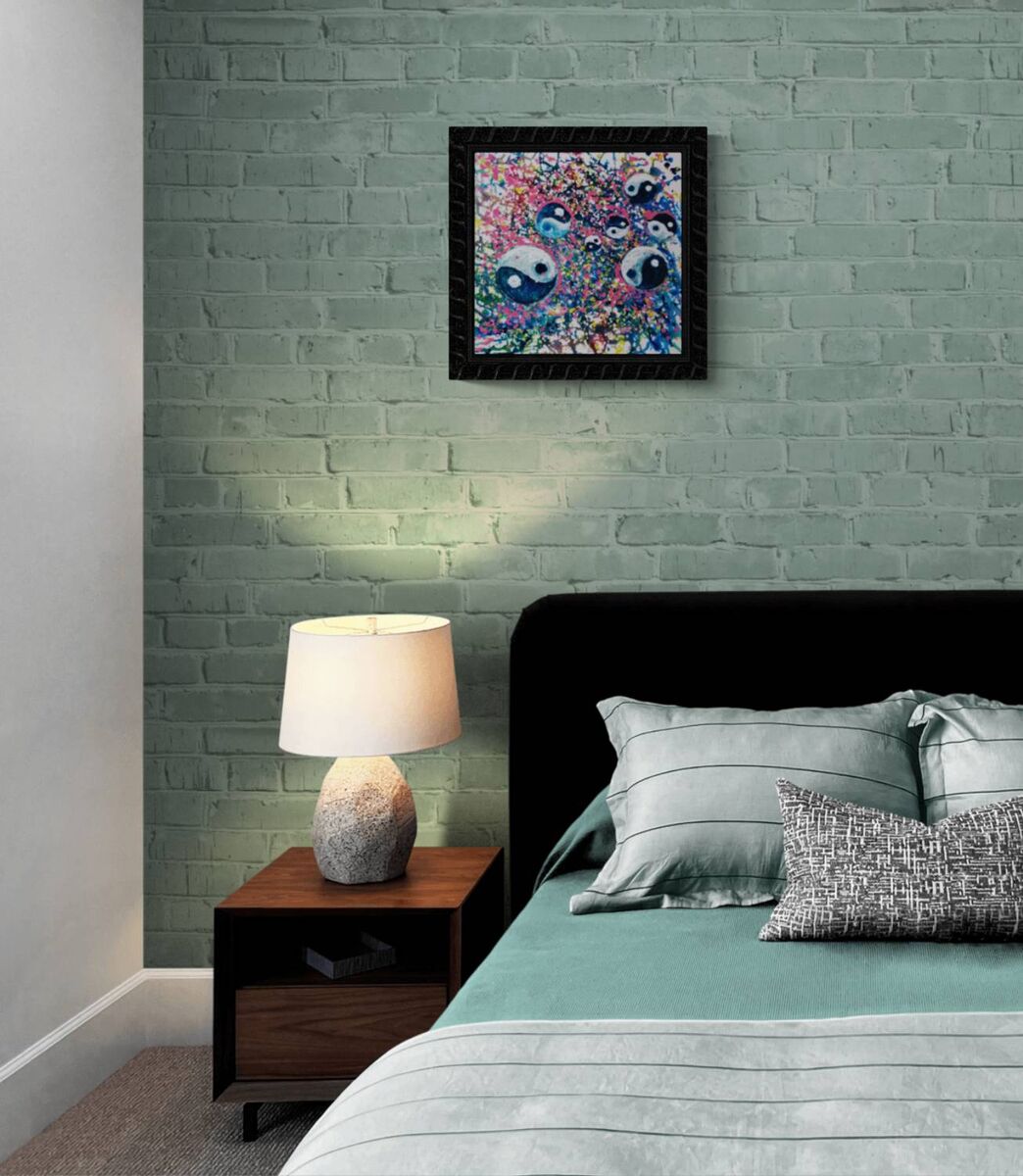 Yin Yang spiritual abstract painting titled Events of Life by Diana Dimova TRAXI featuring a circular blue, white, and soft pink composition for modern luxury interiors. A framed abstract art print featuring colorful eyes hangs on a textured light green brick wall above a bed with gray bedding and a wooden nightstand with a lamp.