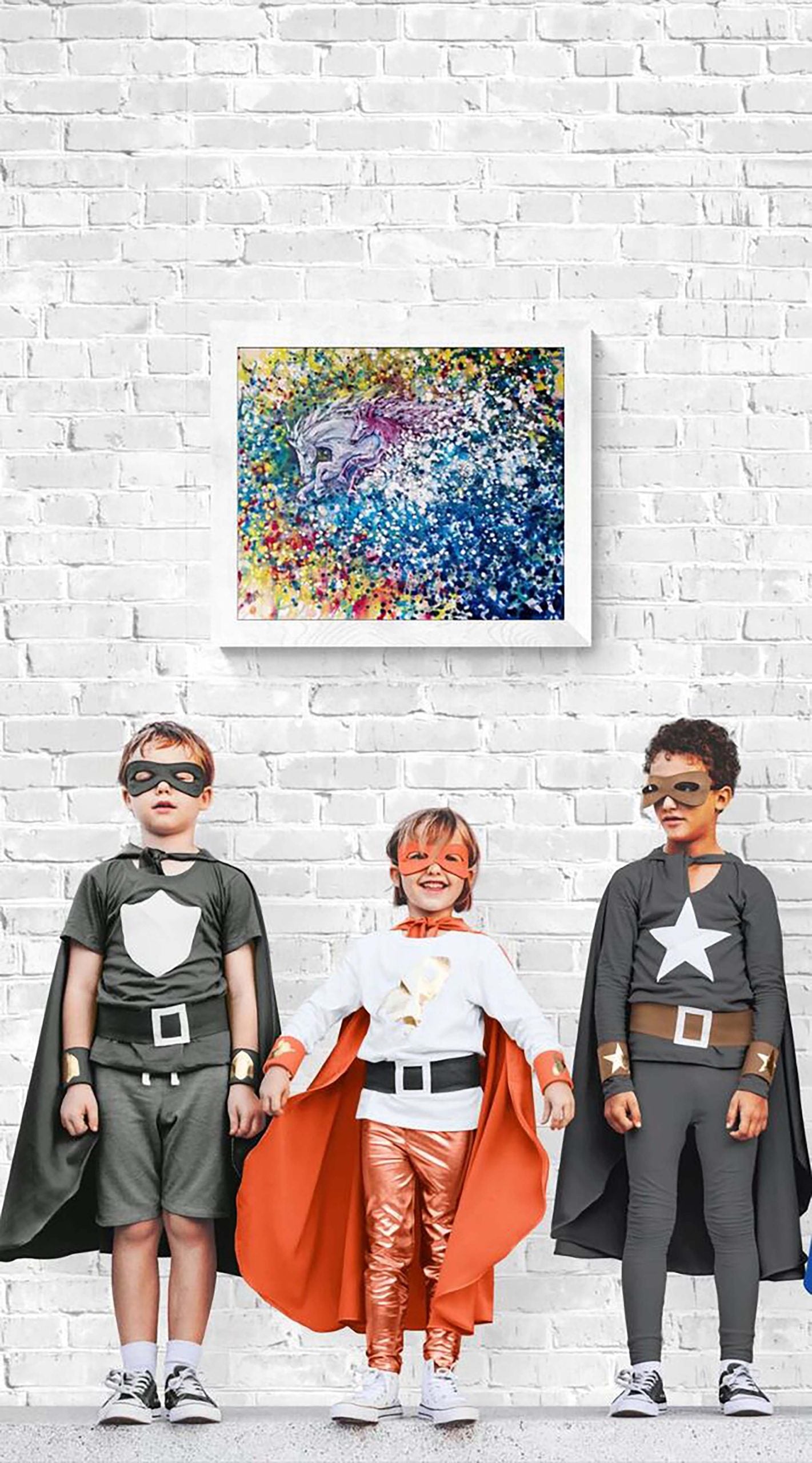 Freedom in color abstract horse original painting by contemporary artist TRAXI, featuring twin horses galloping through a vibrant cosmic nebula sky. Three children dressed as superheroes stand in front of a white brick wall, with a colorful abstract portrait painting hanging on the wall above them.