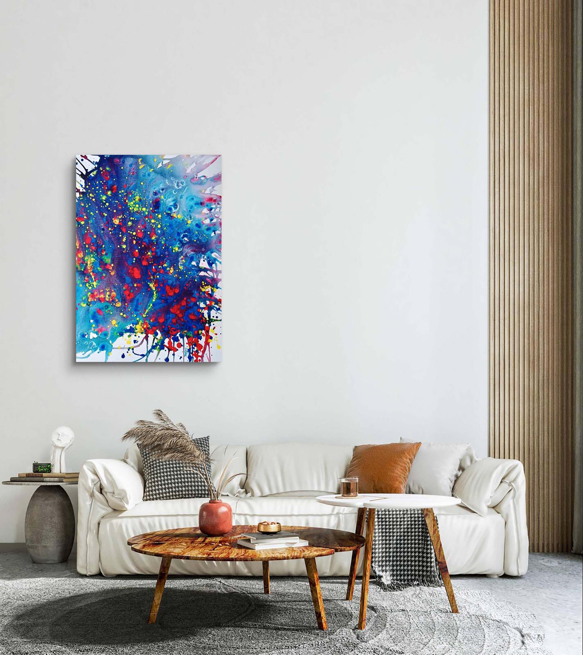 Mood of the Party original vertical abstract fluid acrylic painting with a vibrant blue wave and splashes of red and yellow by Diana Dimova TRAXI ART. A colorful abstract canvas wall art print with blue, red, and white paint splatters, displayed in a modern living room setting above a white sofa.