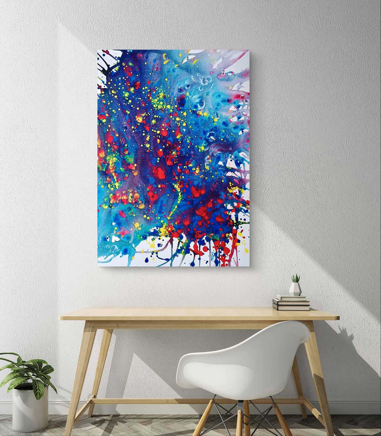 Mood of the Party limited edition premium vertical canvas print with a vibrant blue wave and splashes of red and yellow by Diana Dimova TRAXI ART.A colorful abstract canvas wall art print featuring vibrant blue, red, yellow, and white paint splatters, displayed in a modern room setting above a light wood desk and white chair.