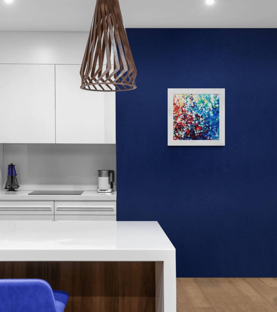 New Beginnings by contemporary artist TRAXI, an original abstract painting featuring blue, red, and gold fluid acrylic pouring techniques exploring emotional transformation. A framed abstract painting with vibrant blue, red, and white brushstrokes hanging on a deep navy blue wall in a modern kitchen setting.