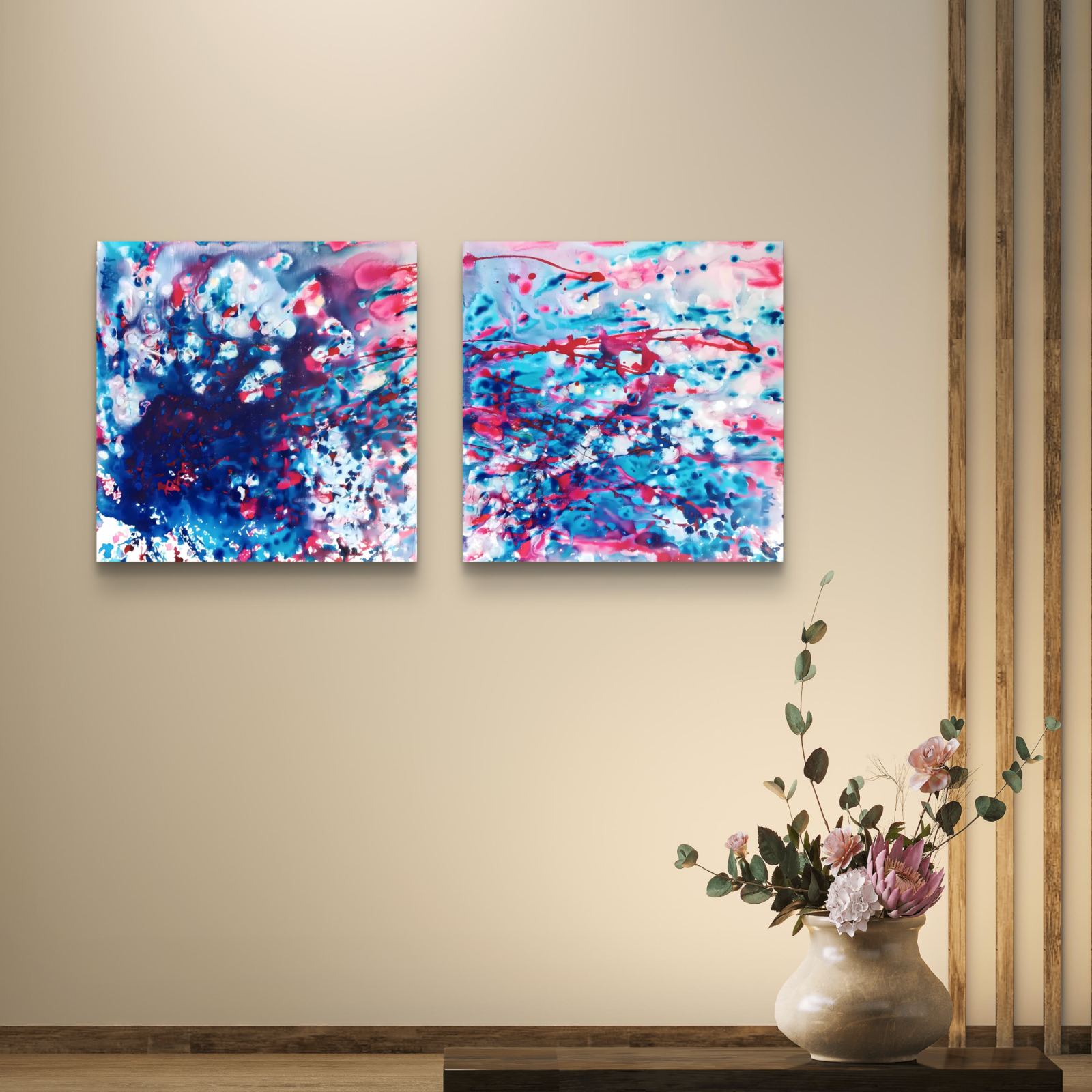 Original abstract diptych Theory of Attraction by Diana Dimova TRAXI, featuring blue, white, and rose tones exploring manifestation and cosmic synchronicity. Two square abstract wall art prints with blue, pink, and white brushstrokes displayed side by side on a beige wall above a console table with a vase of flowers.