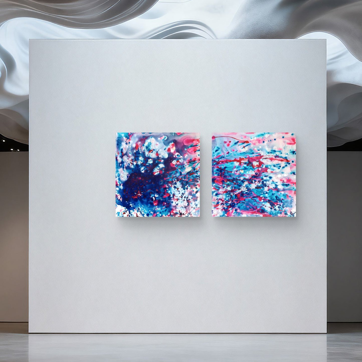 Original abstract diptych Theory of Attraction by Diana Dimova TRAXI, featuring blue, white, and rose tones exploring manifestation and cosmic synchronicity. Two square abstract wall art canvases with vibrant blue, pink, and white paint splatters, displayed side-by-side on a large white panel.