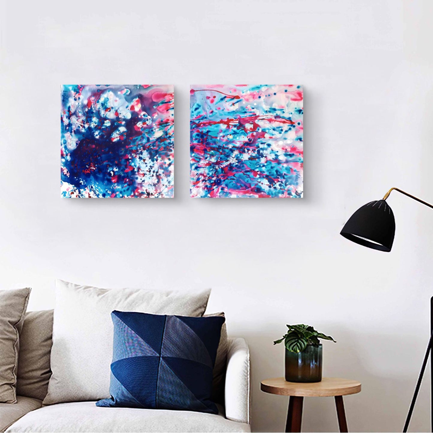 Original abstract diptych Theory of Attraction by Diana Dimova TRAXI, featuring blue, white, and rose tones exploring manifestation and cosmic synchronicity. Two square abstract wall art prints with blue, pink, and white paint splashes displayed above a white sofa in a modern living room setting.