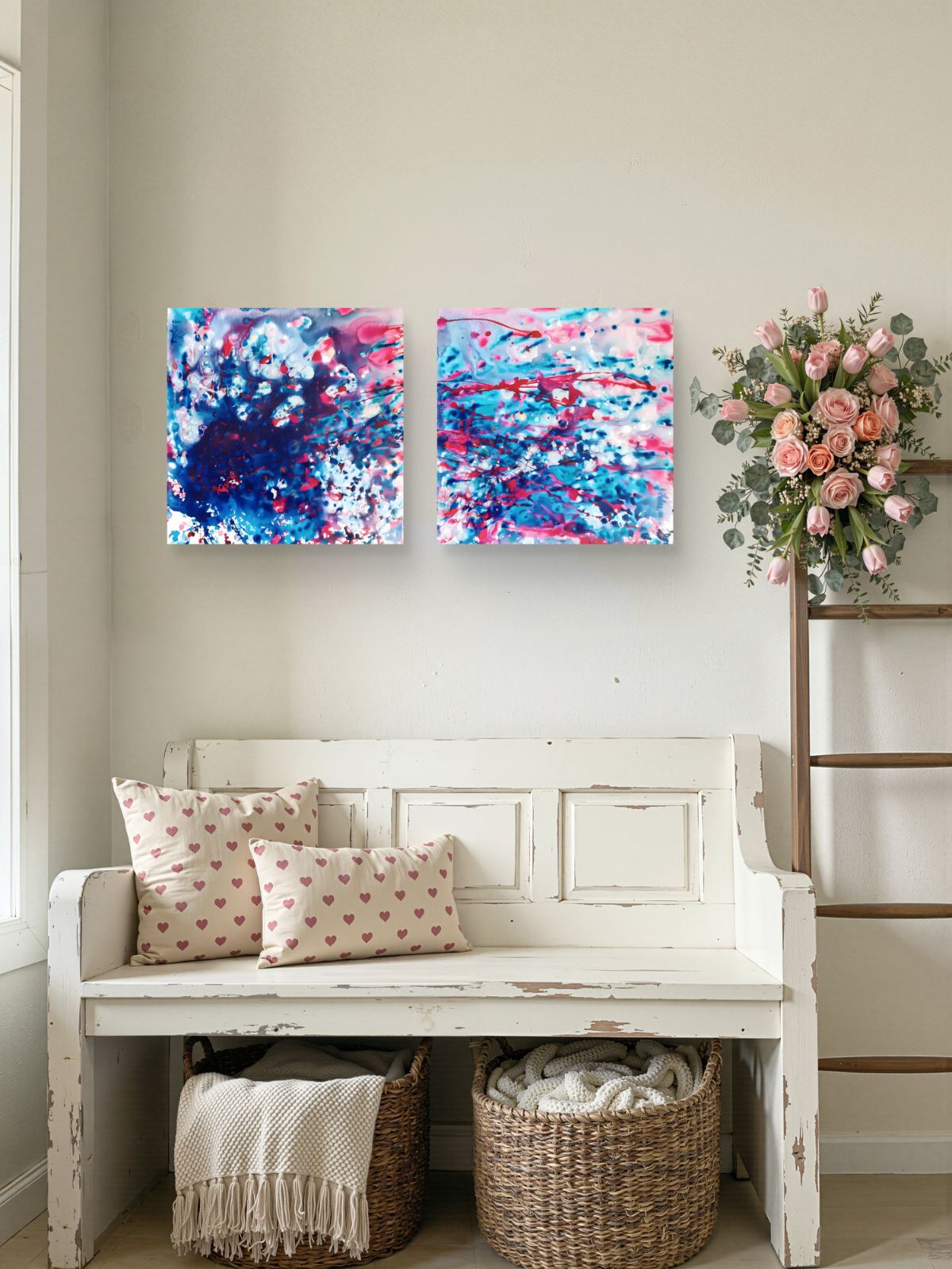 Original abstract diptych Theory of Attraction by Diana Dimova TRAXI, featuring blue, white, and rose tones exploring manifestation and cosmic synchronicity. Two square abstract canvas prints with vibrant blue, pink, and white paint splatters hang on a beige wall above a distressed white wooden bench with heart-patterned pillows, baskets, and a floral arrangement.
