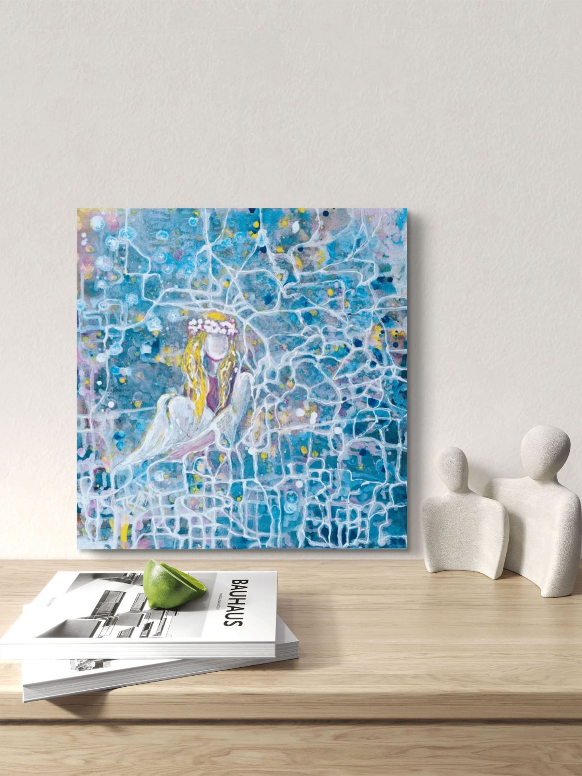 Original abstract figurative painting Connected to the Universe by Diana Dimova TRAXI, featuring a luminous figure emerging from a network of flowing lines. An abstract blue and white painting of a seated figure hangs on a light wall above a wooden shelf with magazines and small white figurines.
