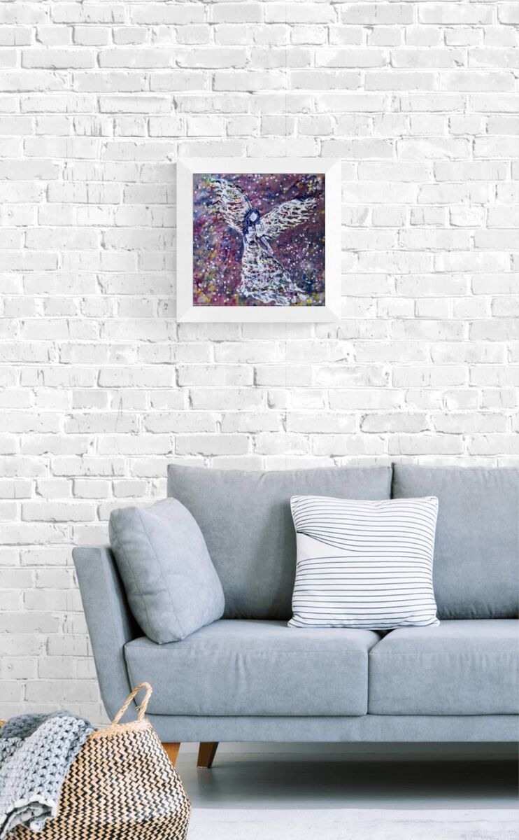 Original abstract figurative painting White Angel by Diana Dimova TRAXI, featuring spiritual symbolism in purple and white tones. A framed abstract art print featuring a purple and blue angel design, displayed on a white brick wall above a light gray sofa with pillows.