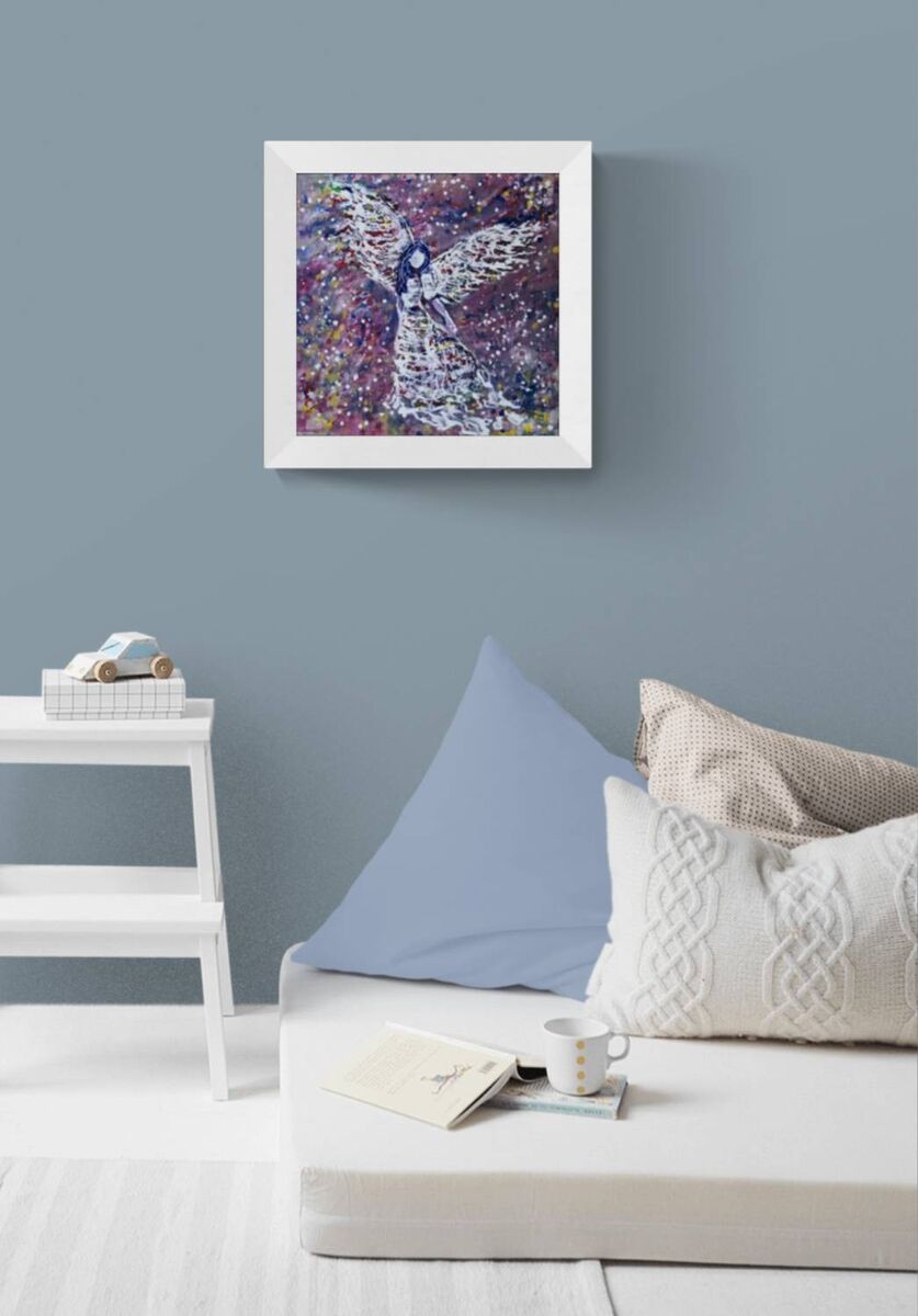 Original abstract figurative painting White Angel by Diana Dimova TRAXI, featuring spiritual symbolism in purple and white tones. A framed abstract art print featuring a stylized angel with outstretched wings in purple, pink, and white tones, displayed on a dusty blue-gray wall above a white daybed with pillows.