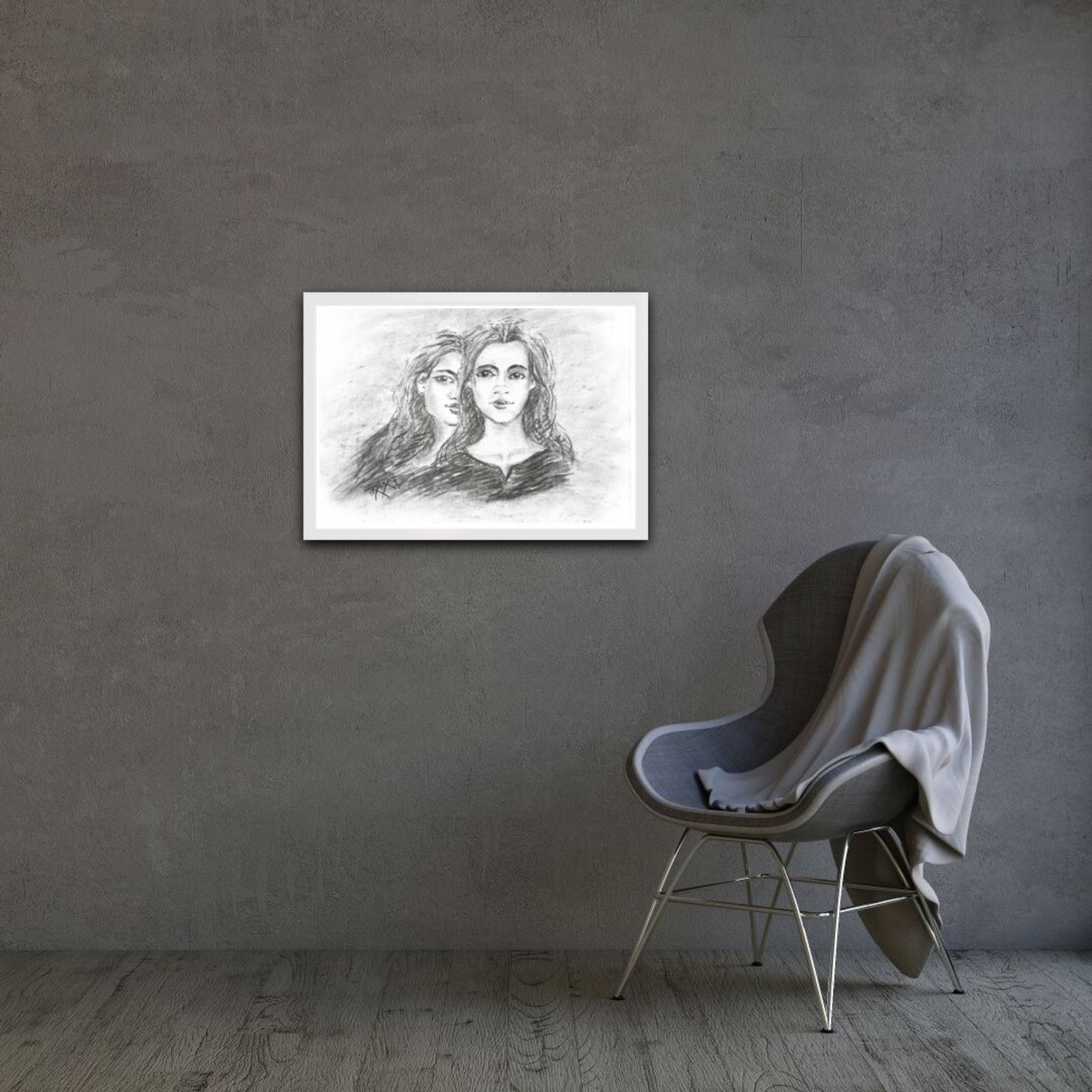 Original monochrome charcoal portrait Duality by Diana Dimova TRAXI, featuring a two-faces woman exploring inner contradiction in black and white tones. A framed black and white pencil sketch of two women's faces hanging on a textured gray wall above a modern gray chair with a draped gray blanket.