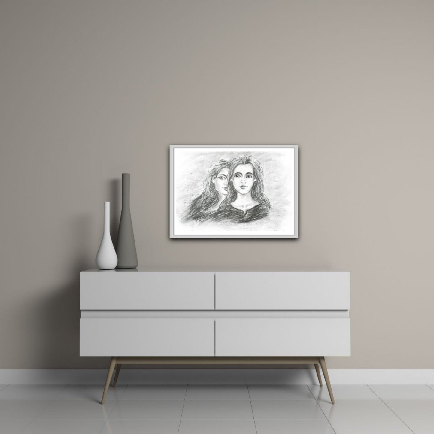 Original monochrome charcoal portrait Duality by Diana Dimova TRAXI, featuring a two-faces woman exploring inner contradiction in black and white tones. A framed black and white pencil sketch of two women's faces hangs on a beige wall above a modern white sideboard with decorative vases.