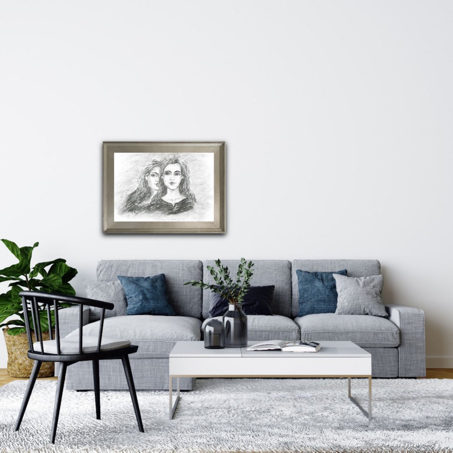Original monochrome charcoal portrait Duality by Diana Dimova TRAXI, featuring a two-faces woman exploring inner contradiction in black and white tones. A framed black and white sketch print of two women hanging on a white wall above a modern gray sofa in a styled living room.