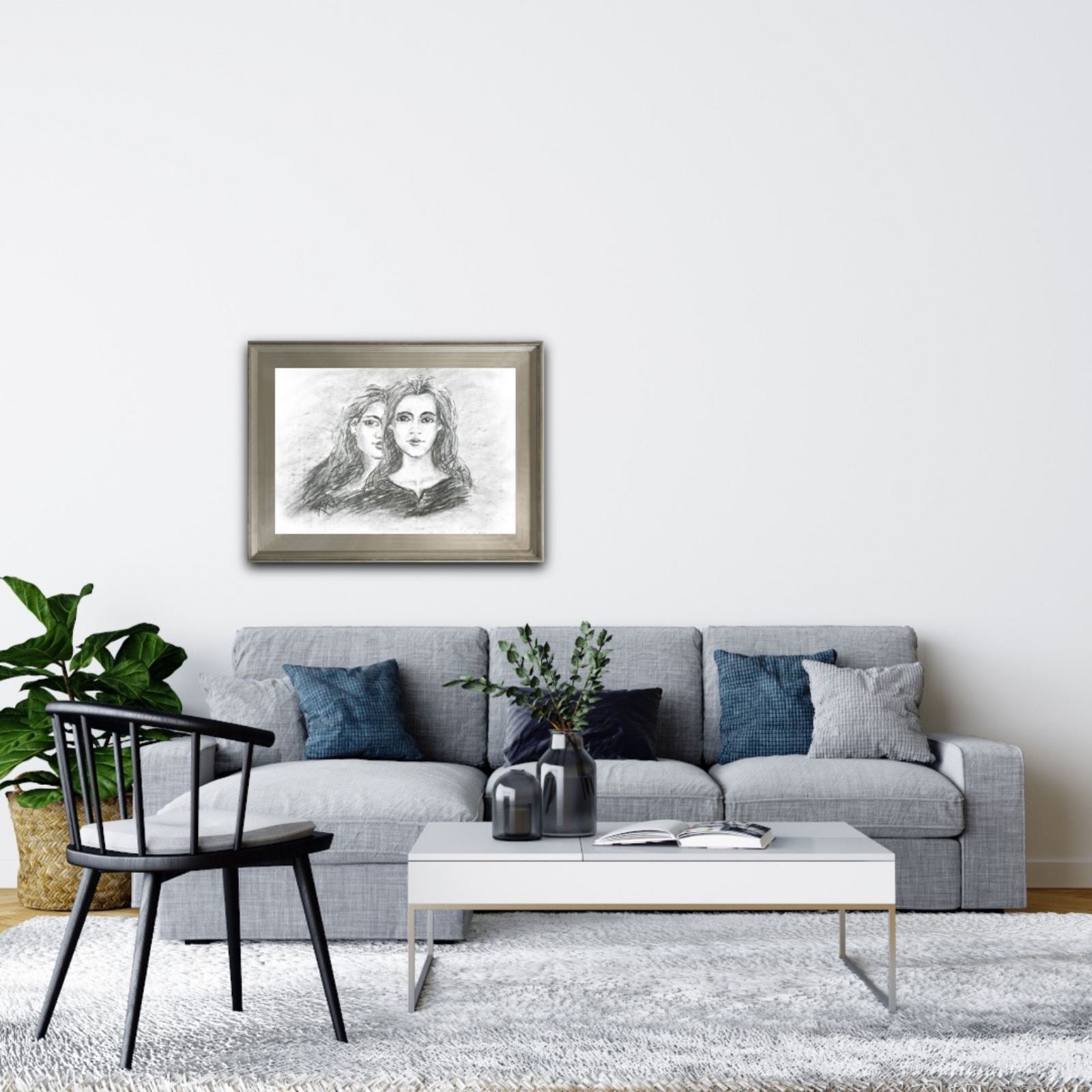 Original monochrome charcoal portrait Duality by Diana Dimova TRAXI, featuring a two-faces woman exploring inner contradiction in black and white tones. A framed black and white sketch print of two women hanging on a white wall above a modern gray sofa in a styled living room.