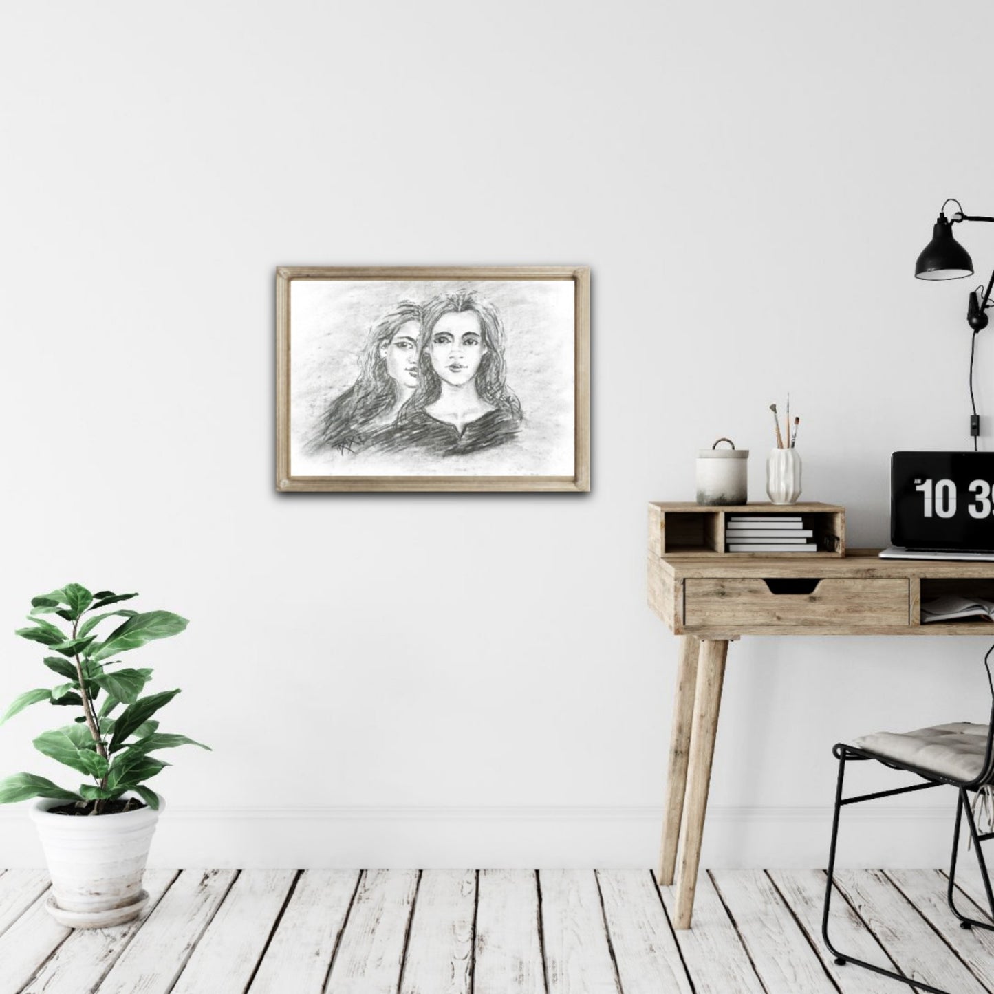 Original monochrome charcoal portrait Duality by Diana Dimova TRAXI, featuring a two-faces woman exploring inner contradiction in black and white tones. Framed artwork of two faces on a wall above a wooden desk with a plant and lamp.