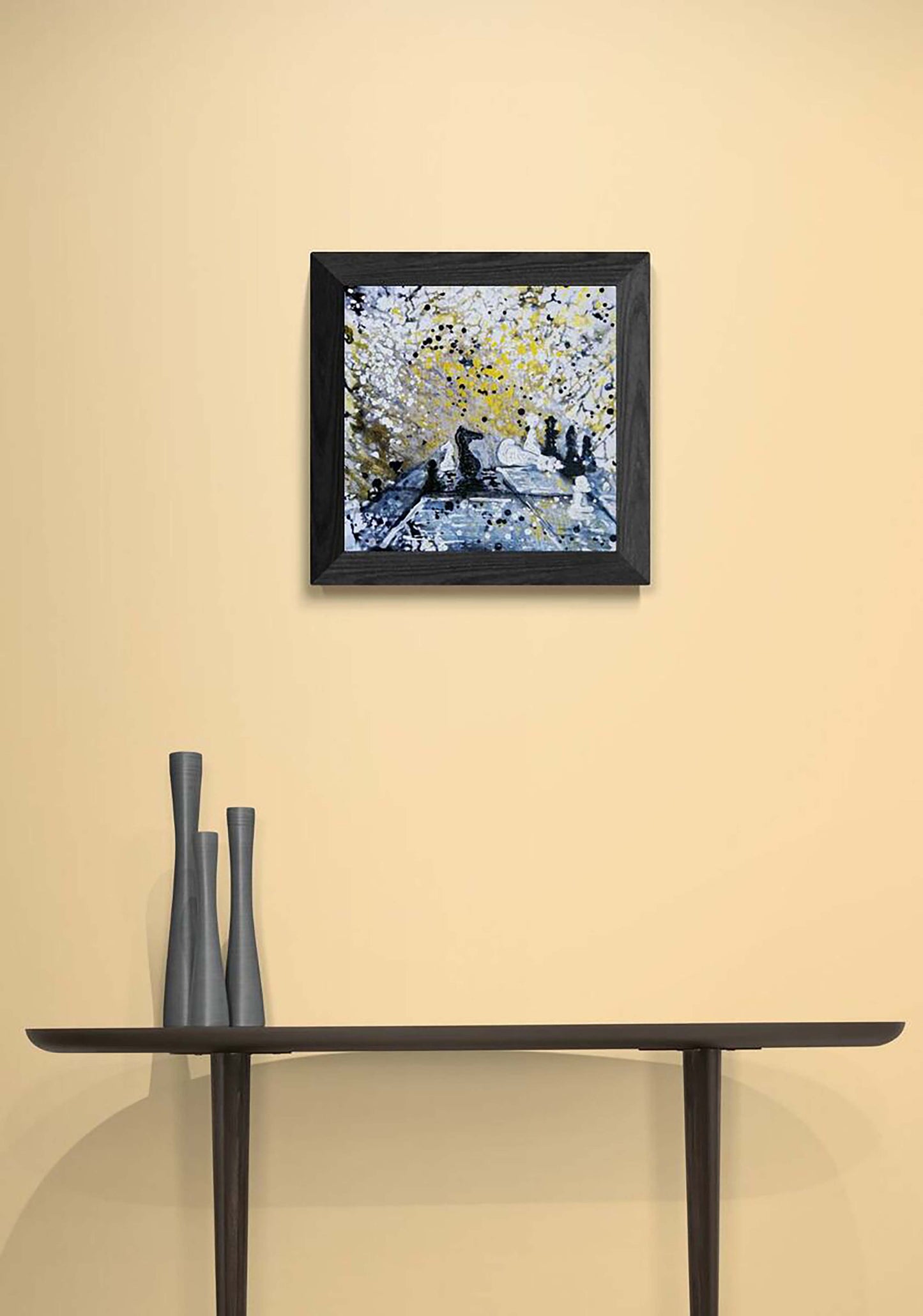 Original symbolic abstract painting Black Wins Again by Diana Dimova TRAXI, featuring chess elements in white, black, and gold tones. A framed abstract painting with yellow, white, and blue brushstrokes hangs on a beige wall above a dark console table with three gray vases.