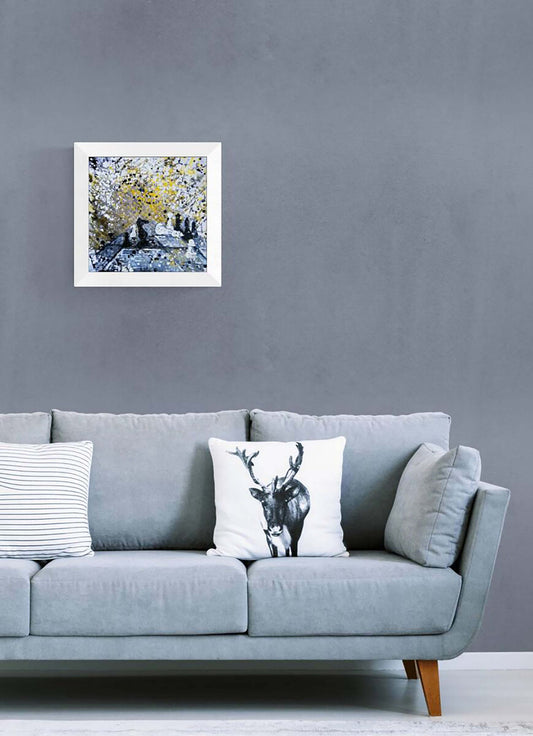 Original symbolic abstract painting Black Wins Again by Diana Dimova TRAXI, featuring chess elements in white, black, and gold tones. A framed abstract landscape art print with blue, white, and yellow tones hangs on a textured gray wall above a light blue-gray sofa with decorative throw pillows.
