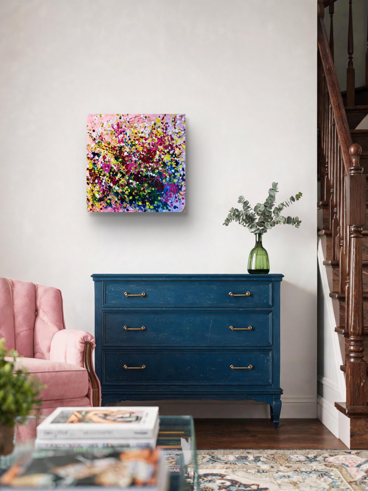 Original abstract painting Summer Garden Flowers by Diana Dimova TRAXI, featuring a colorful floral bouquet in vibrant yellow, pink, and orange tones. A colorful abstract floral canvas print is displayed on a white wall above a dark blue wooden dresser in a styled living room setting.