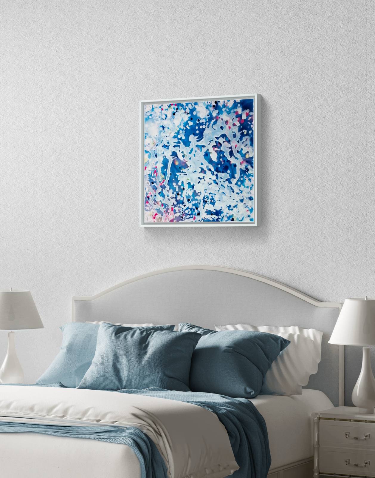 Original spiritual abstract painting Prayer by Diana Dimova TRAXI, featuring a white angel and protective wings in white and blue tones. A framed abstract art print featuring blue, white, and pink brushstrokes, displayed on a textured light gray wall above a bed with blue and white bedding.