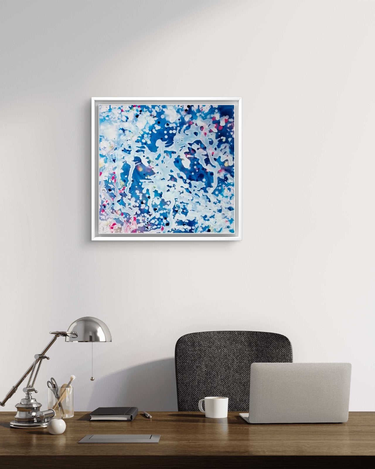 Original spiritual abstract painting Prayer by Diana Dimova TRAXI, featuring a white angel and protective wings in white and blue tones. A square framed abstract art print with blue, white, and pink brushstrokes, displayed on a white wall above a wooden desk with a laptop, lamp, and chair.