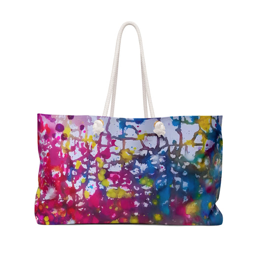 Paintings of happiness beach bag featuring vibrant wearable art inspired by the Paintings of Happiness series by Diana Dimova TRAXI. A rectangular tote bag with a vibrant multicolor paint splatter pattern in pink, blue, yellow, and purple, featuring white rope handles on a solid white background.