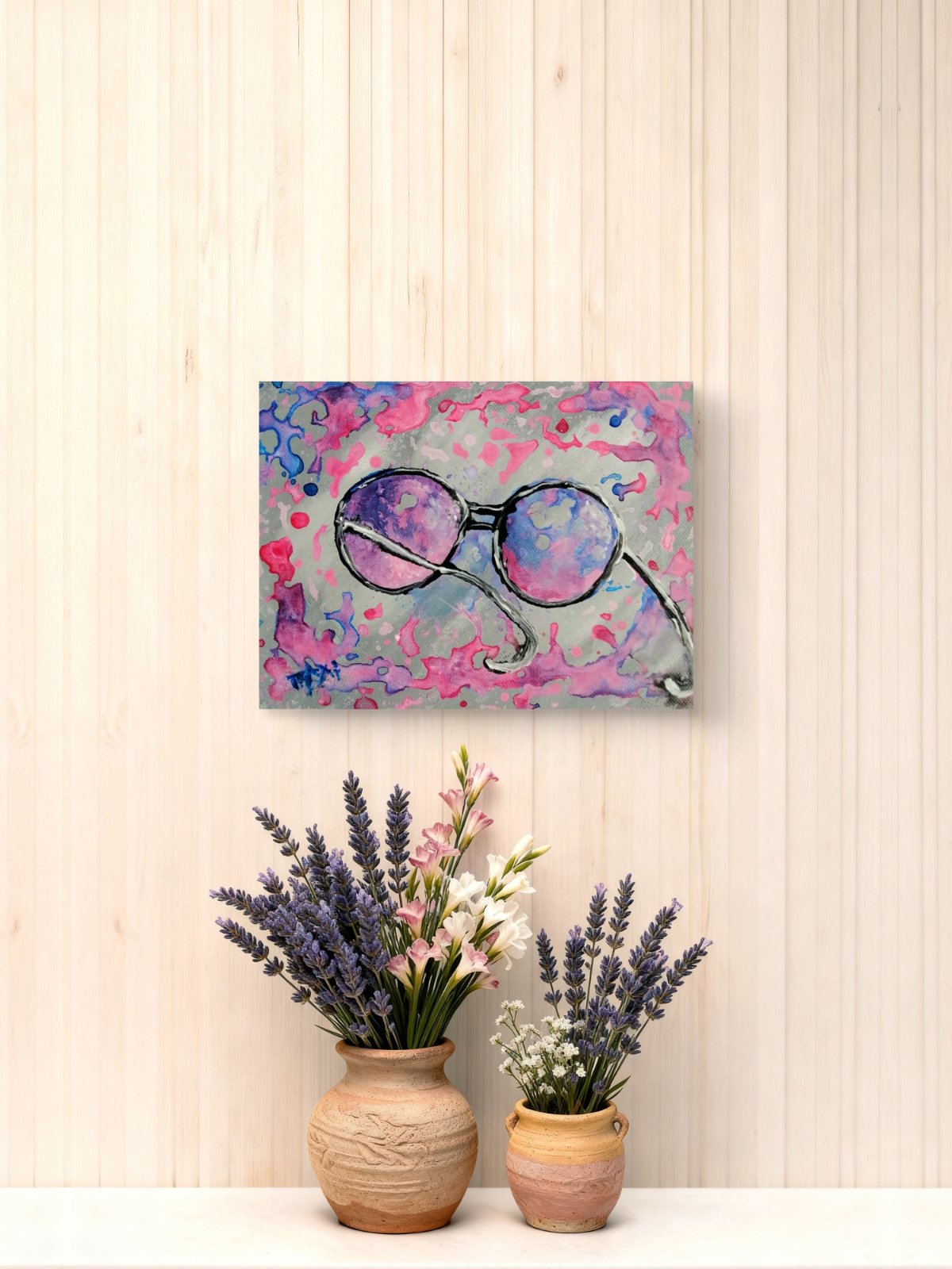 Pink glasses original abstract painting by contemporary artist TRAXI, featuring vibrant fluid acrylics and a joyful, perfect gift idea . A square canvas art print featuring an abstract painting of round sunglasses with purple and pink lenses, displayed on a light wood-paneled wall above two small potted lavender plants in terracotta vases.