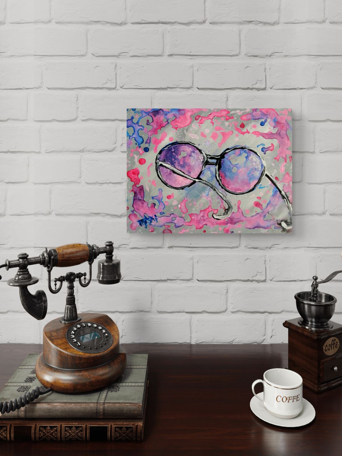 Pink glasses original abstract painting by contemporary artist TRAXI, featuring vibrant fluid acrylics and a joyful, perfect gift idea . A square canvas wall art print featuring a colorful abstract painting of round sunglasses, displayed on a white brick wall above a dark wooden table styled with a vintage rotary phone, a coffee grinder, and a coffee cup.