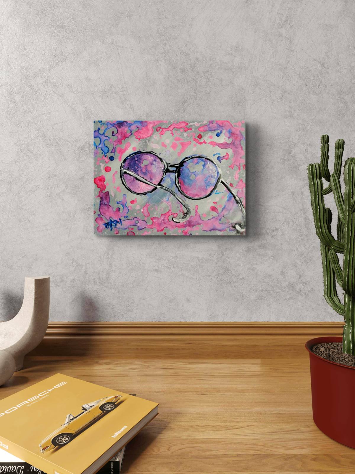Pink glasses original abstract painting by contemporary artist TRAXI, featuring vibrant fluid acrylics and a joyful, perfect gift idea . A square wall art print featuring an abstract painting of round sunglasses with purple and pink lenses, displayed on a light gray textured wall above a wooden floor next to a potted cactus.