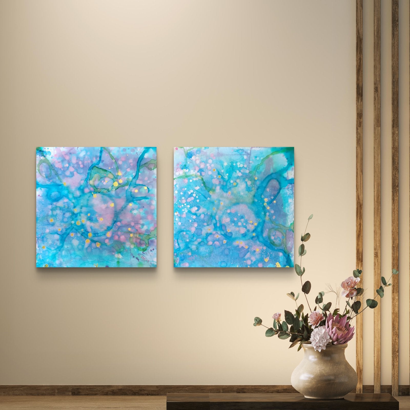 Original abstract diptych painting titled 'Rearrangement' by TRAXI, featuring textured layers in dialogue. The artwork explores themes of renewal, transition, and reconstruction through contemporary abstract expressionism. Two square abstract wall art canvases with swirling blue, purple, and teal patterns hanging side by side on a beige wall, with a small vase of flowers below.
