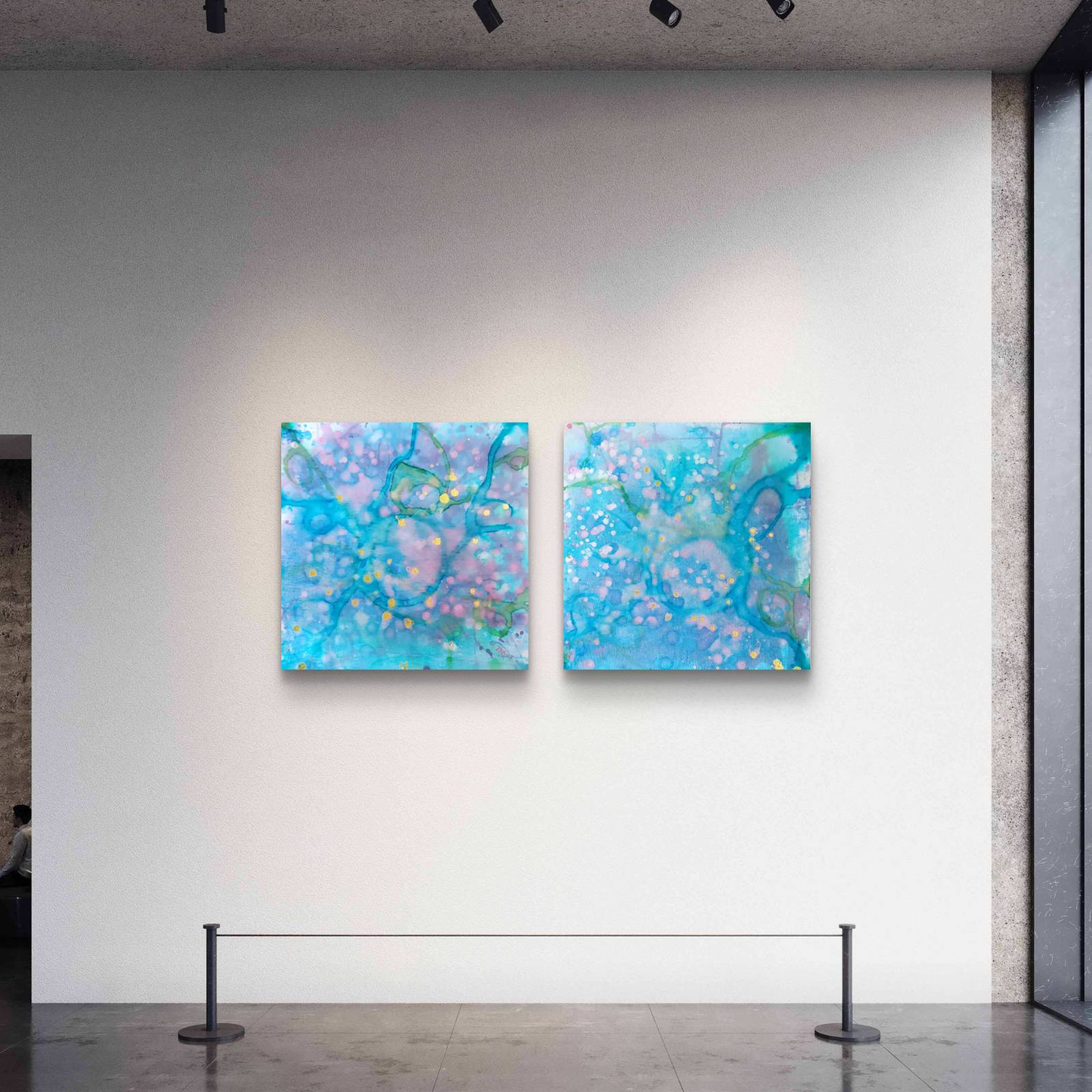 Original abstract diptych painting titled 'Rearrangement' by TRAXI, featuring textured layers in dialogue. The artwork explores themes of renewal, transition, and reconstruction through contemporary abstract expressionism. Two square abstract wall art prints with swirling blue, aqua, purple, and white patterns hang side by side on a white gallery wall. The space includes a dark floor, track lighting, and a rope barrier in the foreground.
