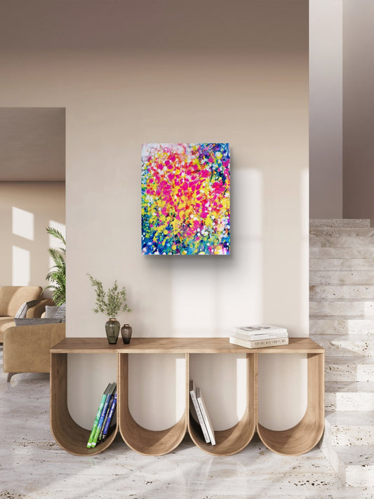 Summer flowers limited edition canvas print by contemporary artist TRAXI, featuring vibrant abstract fluid acrylic colors and warm seasonal energy in a 50x60 cm format. A colorful abstract canvas print with vibrant pink, yellow, blue, and green brushstrokes, displayed on a beige wall above a modern wooden console table in a minimalist interior setting.