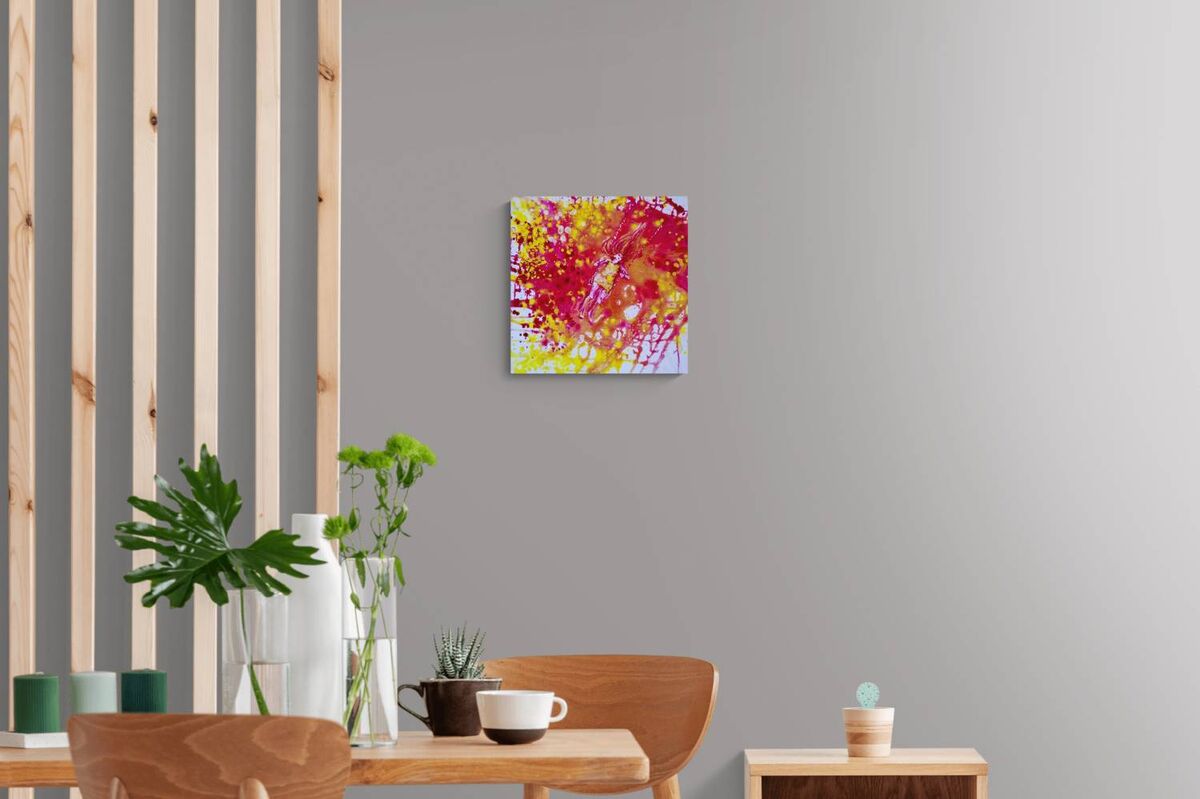 Sunshine Swing original fluid acrylic abstract painting by Diana Dimova TRAXI ART. Finalist Award winner 2022. A square abstract wall art print with vibrant red, yellow, and pink brushstrokes hanging on a light gray wall in a modern dining room setting.