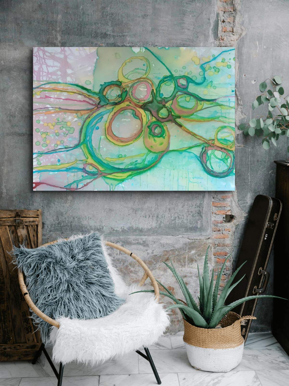 Original abstract painting titled 'The Balance' by TRAXI featuring serene textures and organic rhythms. The artwork represents the culmination of the series States of Becoming, exploring harmony, nature, and spiritual equilibrium. An abstract canvas wall art print featuring flowing green, yellow, and pink brushstrokes, displayed on a textured gray concrete wall above a modern chair with a fluffy throw pillow.