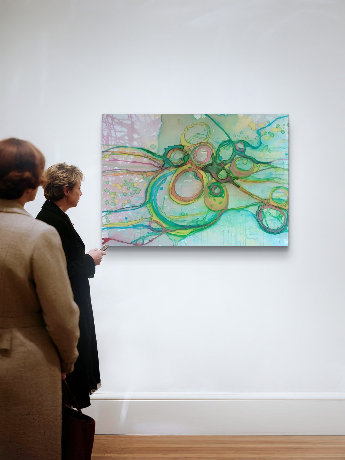 Original abstract painting titled 'The Balance' by TRAXI featuring serene textures and organic rhythms. The artwork represents the culmination of the series States of Becoming, exploring harmony, nature, and spiritual equilibrium. An abstract painting with flowing green, yellow, and teal lines over a pale aqua and pink background, displayed on a white gallery wall. Two people are standing in the foreground, viewing the artwork in a gallery setting.