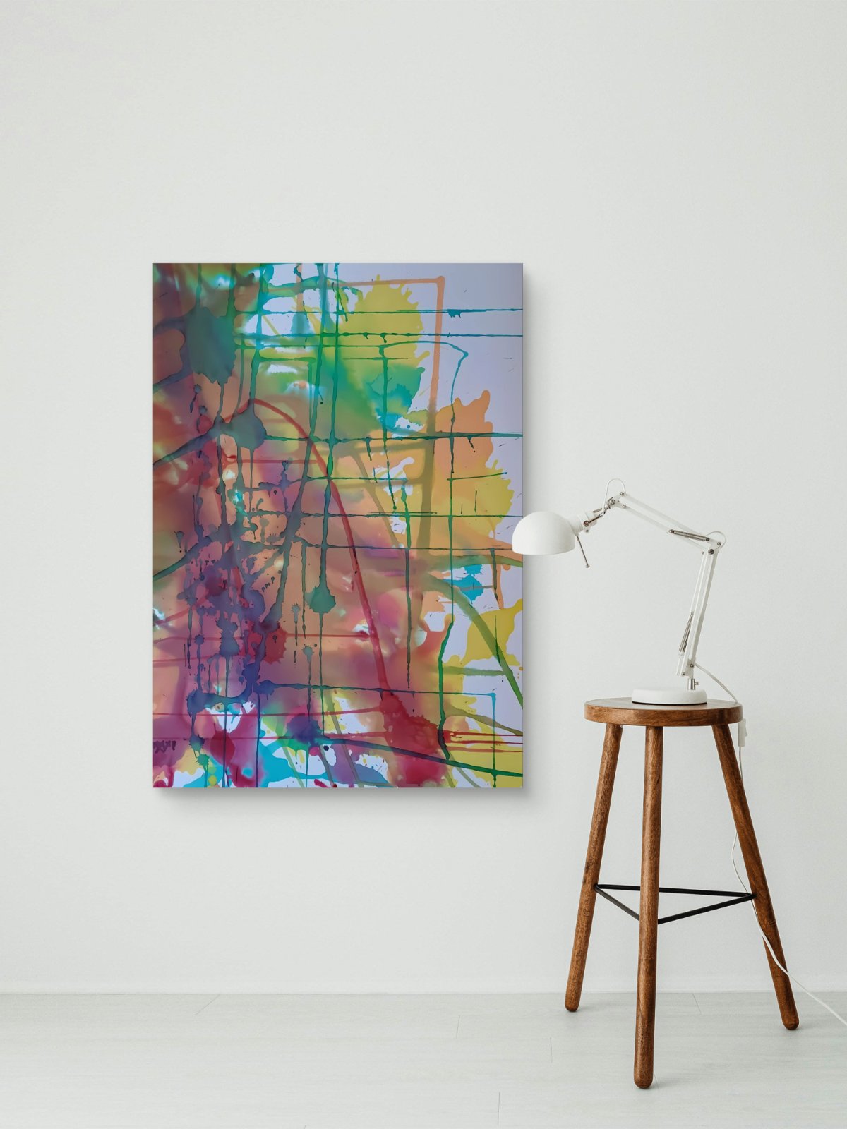 Original abstract painting titled 'The Fracture' by TRAXI, featuring expressive textures and dynamic movement. The artwork explores themes of change and emotional transformation through contemporary abstract expressionism. An abstract canvas wall art print with colorful paint splatters and drips, displayed on a white wall next to a wooden stool with a white desk lamp.