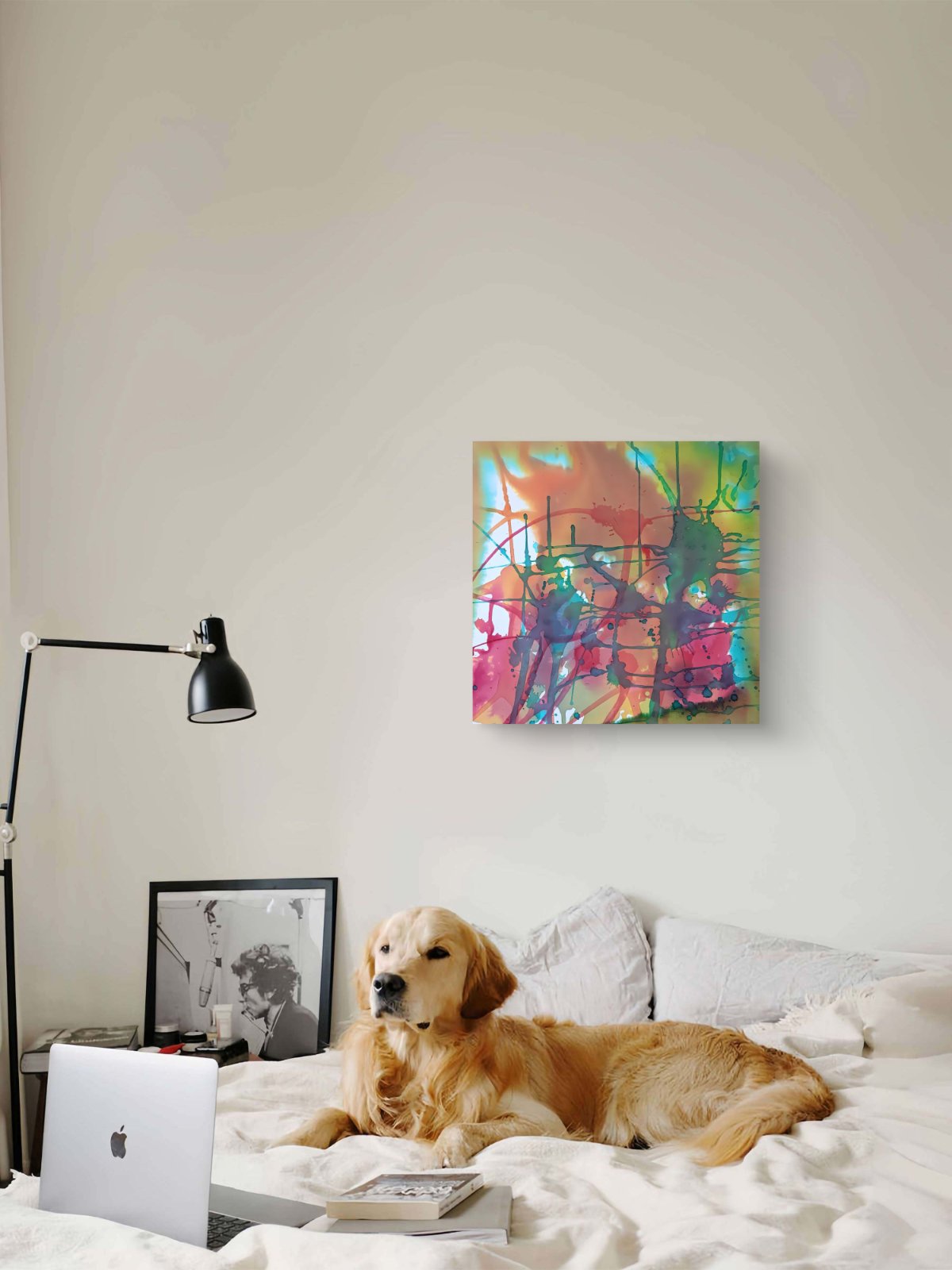 Original abstract painting titled 'The Noise' by TRAXI, featuring fragmented forms and energetic movement. The artwork explores urban life and contemporary chaos through abstract expressionism. A golden retriever dog lies on a white bed in a modern bedroom, with a colorful abstract canvas print hanging on the wall above. A black desk lamp, an open laptop, and a framed picture are visible on the bedside table.