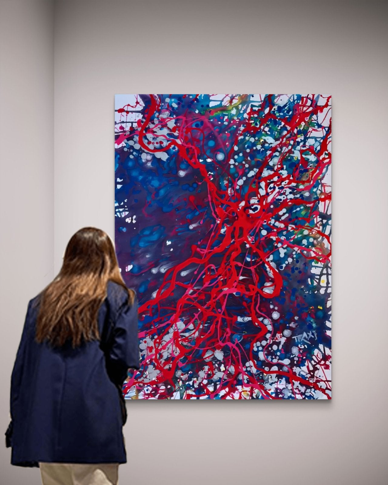 Blood Connection original red, blue, and silver abstract painting by Diana Dimova TRAXI ART. Winner of First Prize in San Francisco 2024. A woman in a navy blue jacket stands with her back to the camera, looking at a large abstract canvas painting featuring vibrant red splatters and lines over a deep blue background.