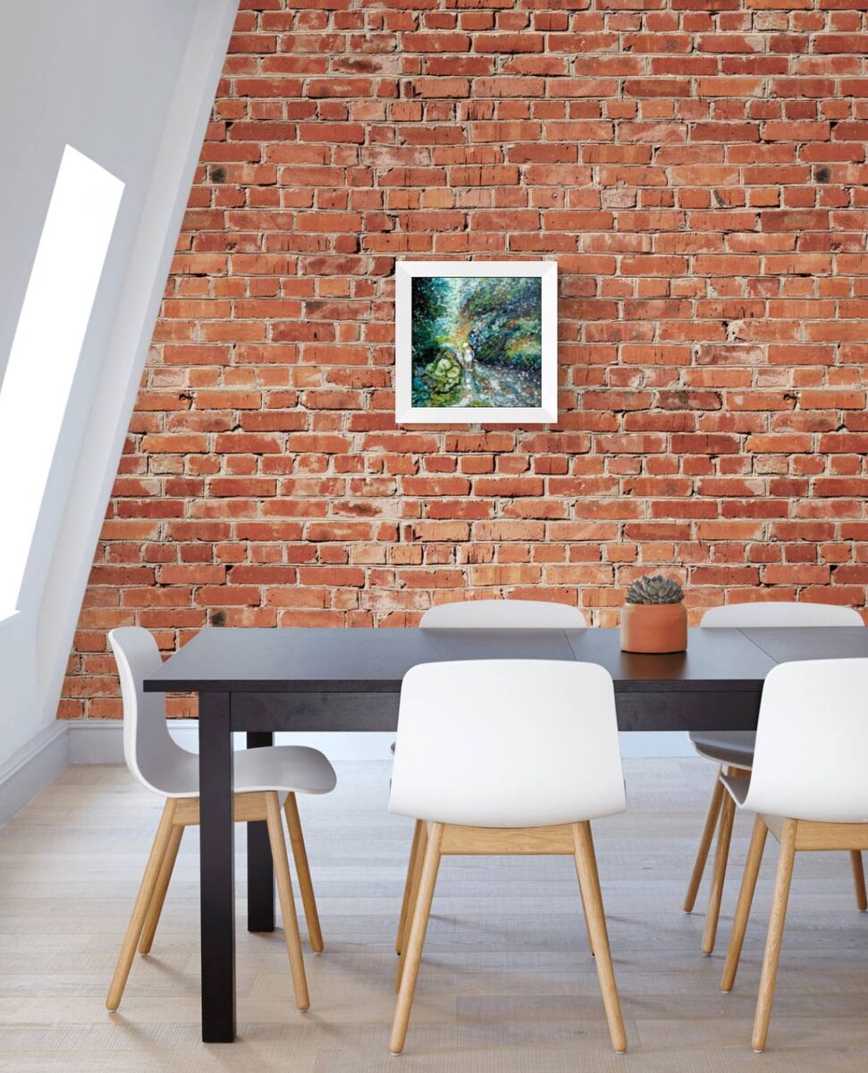 A framed art print depicting a lush green forest hangs on a red brick wall above a modern dining table and white chairs. By the River original impressionist oil painting with fresh green and white tones depicting a young girl by the river by Diana Dimova TRAXI ART.