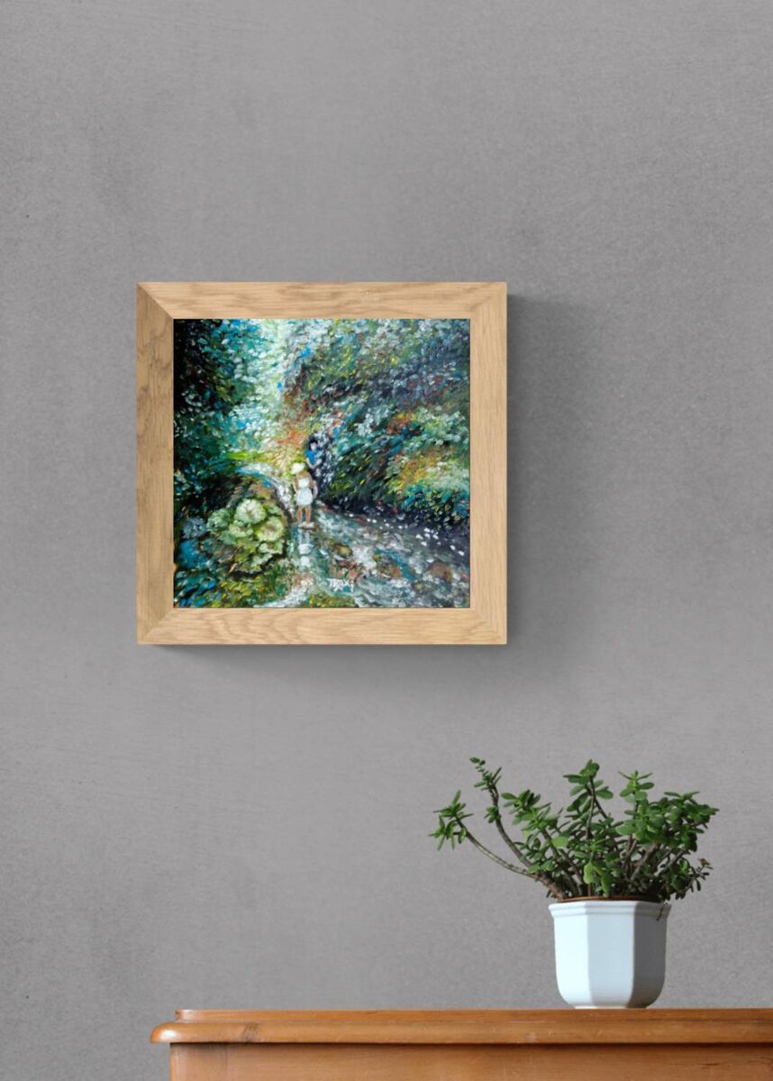 A framed square art print featuring an impressionistic forest scene in shades of green, blue, and white, displayed on a textured gray wall above a wooden console table with a potted green plant. By the River original impressionist oil painting with fresh green and white tones depicting a young girl by the river by Diana Dimova TRAXI ART.