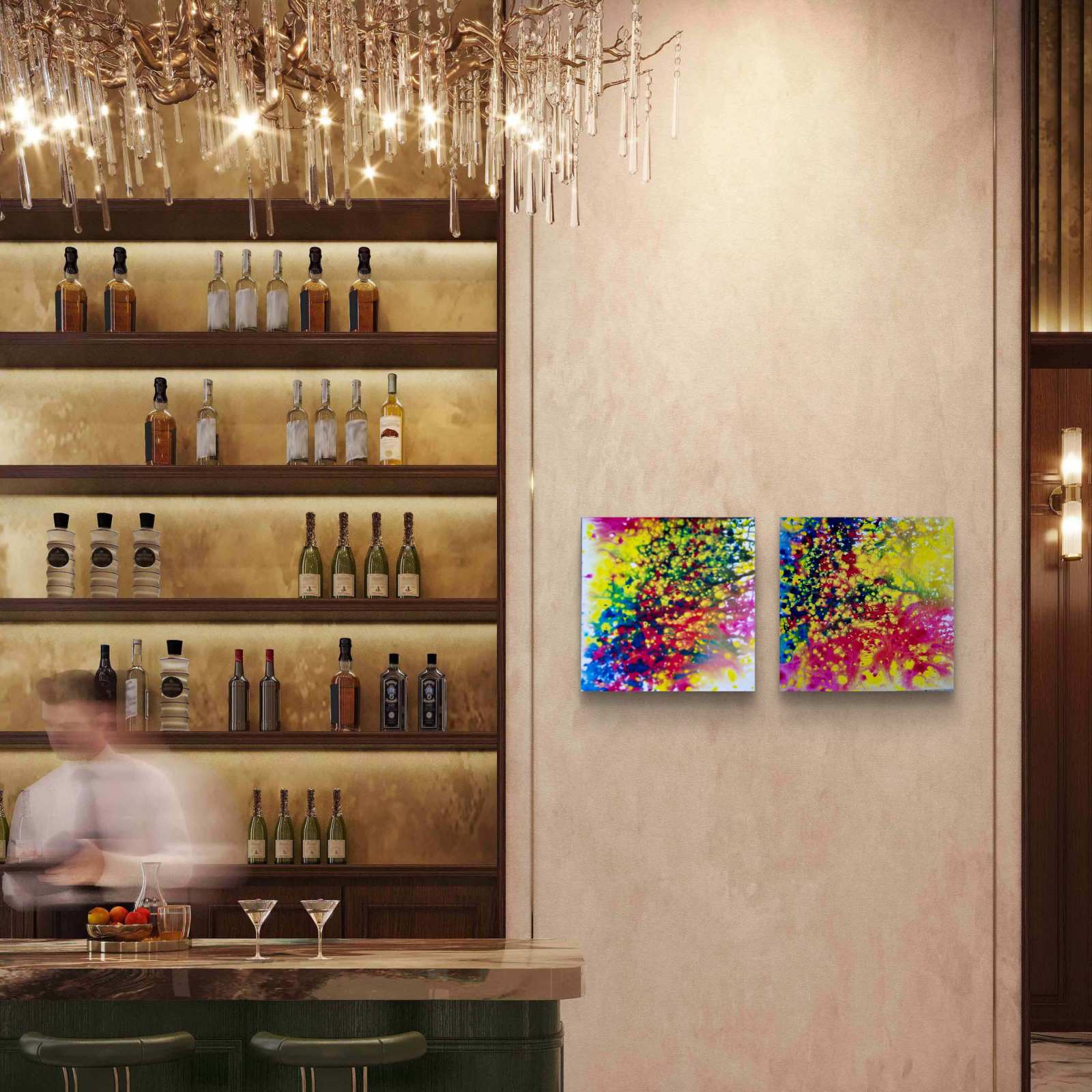 Fires Set original fluid acrylic abstract diptych in blue, red, orange, and yellow by Diana Dimova TRAXI ART. Finalist Award winner 2025. Two square abstract paintings with vibrant multicolor paint splatters hang on a beige wall in a modern bar setting with a chandelier, shelves of bottles, and a blurred bartender in the background.
